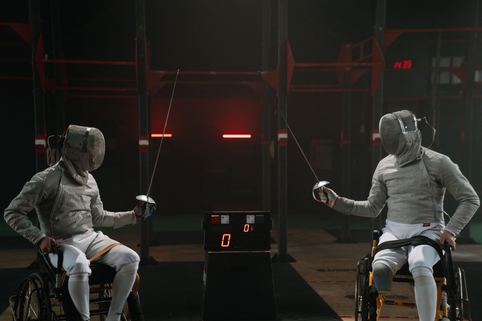 Two male wheelchair fencers in an intense match indoors, showcasing skill and determination.