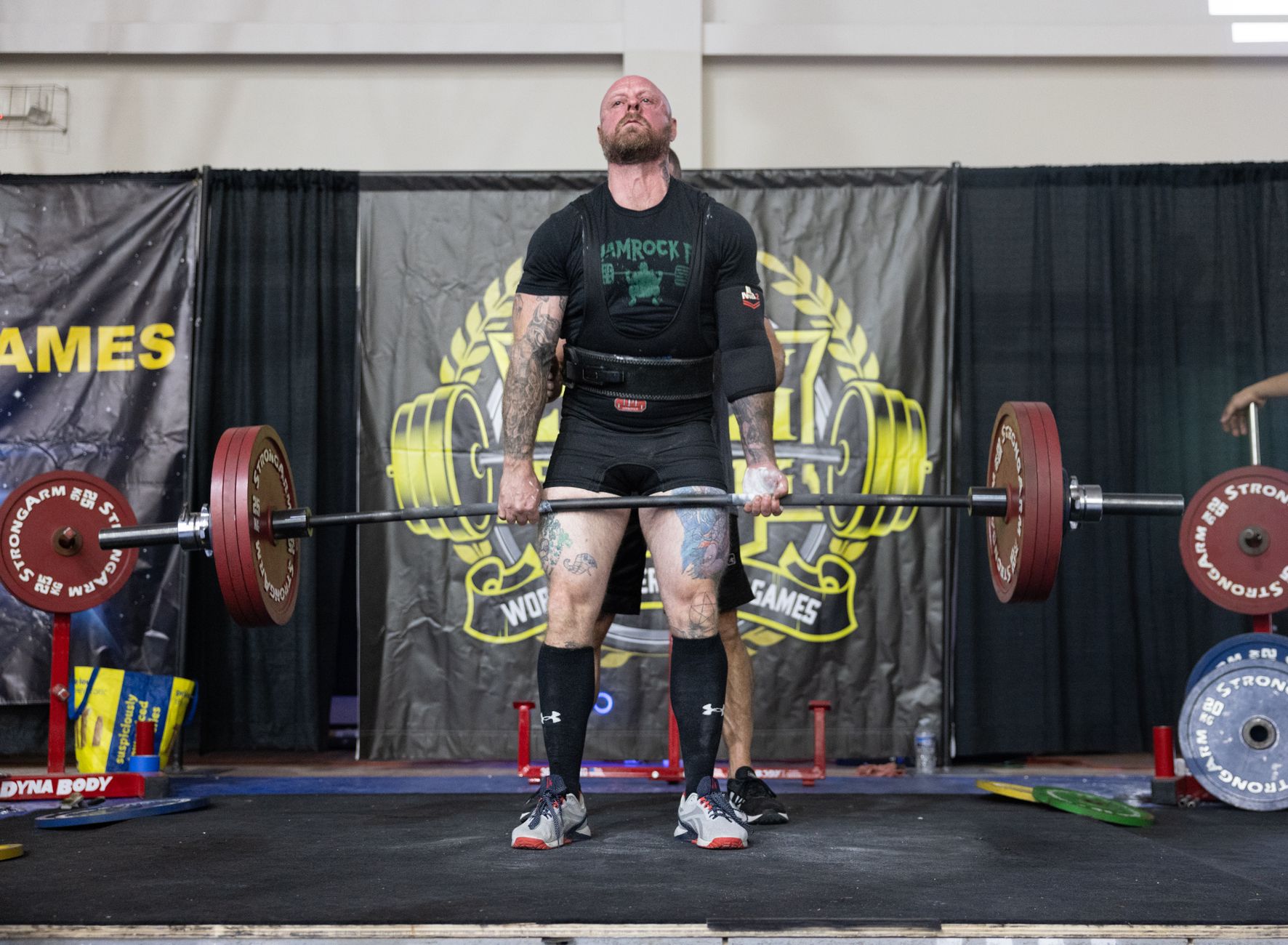 A muscular man performing a deadlift during a strongman event indoors.