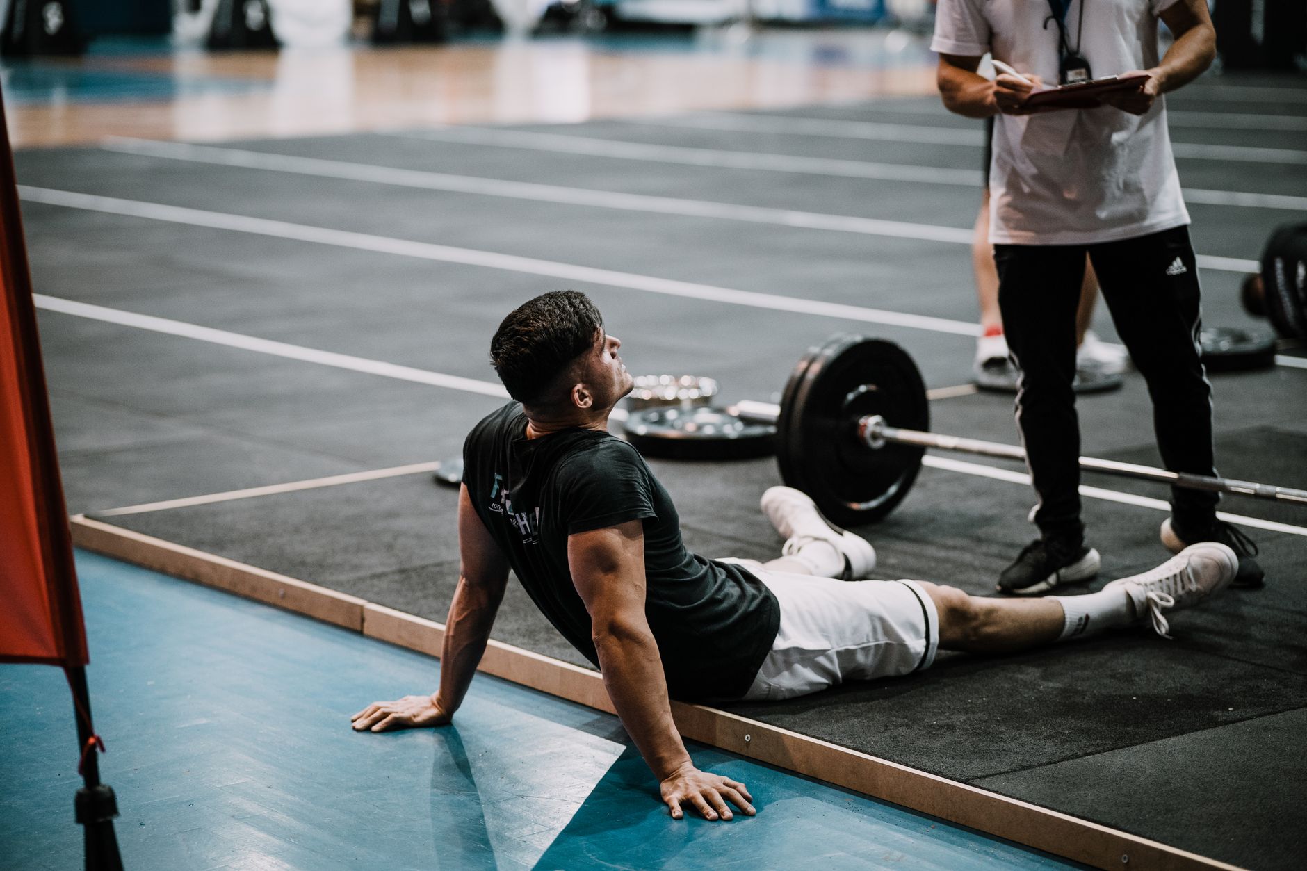 A young man sits on the gym floor after an intense lifting session, demonstrating athletic endurance.