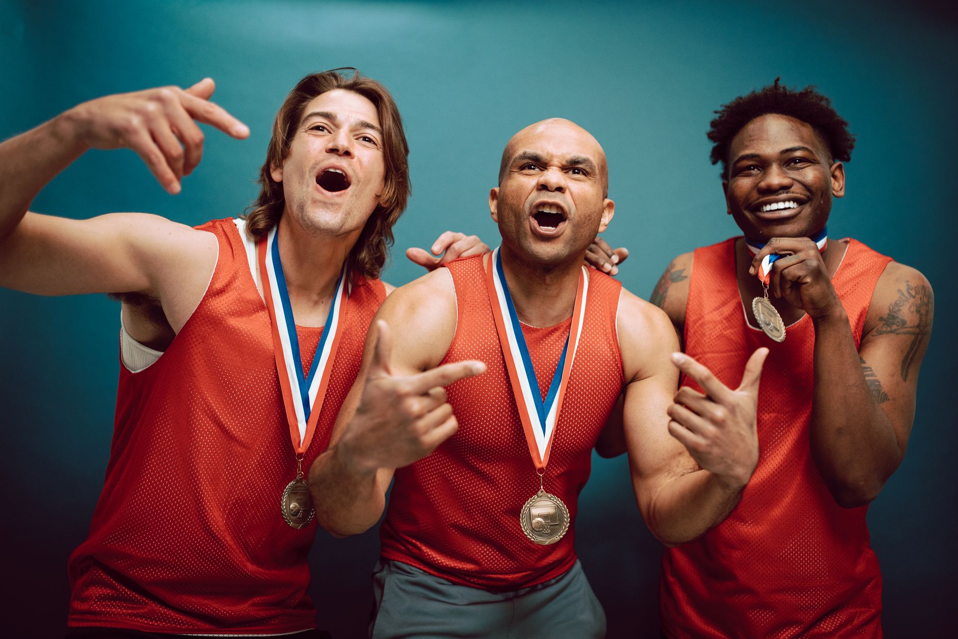 Three male athletes in red jerseys celebrating with medals indoors.