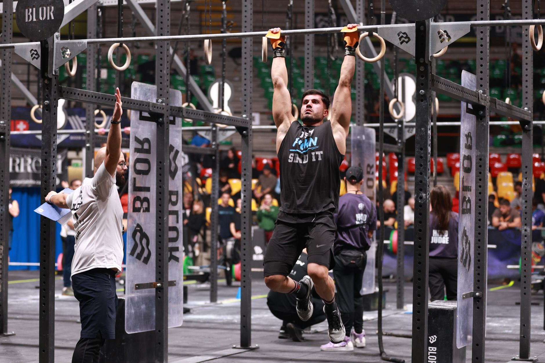 Athlete performing pull-ups during a competitive CrossFit event indoors.