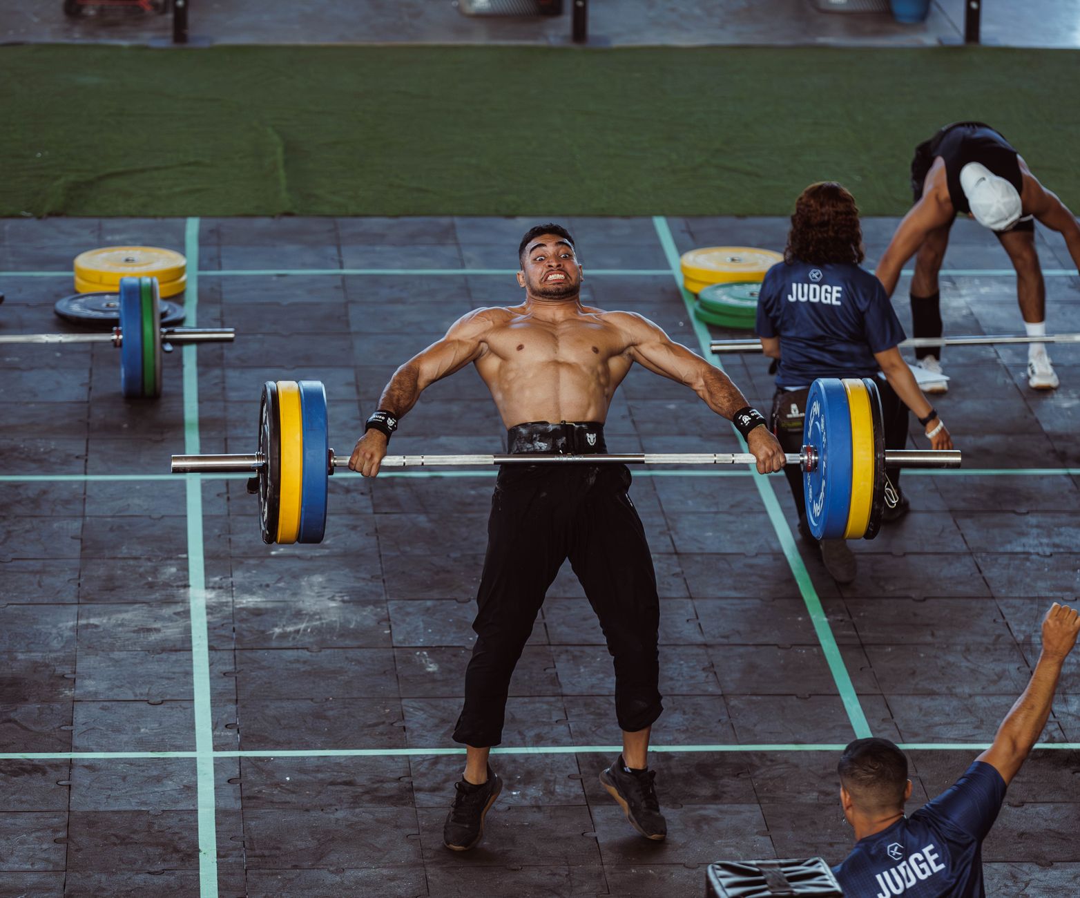 Male athlete executing a clean and jerk lift during a weightlifting competition, showcasing strength and focus.