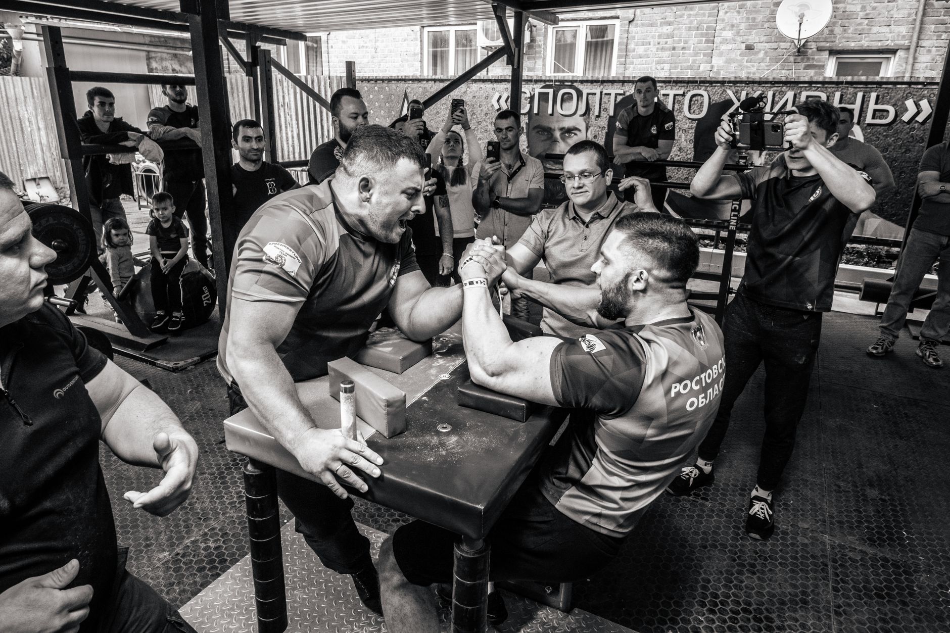Black and white photo capturing a dynamic arm wrestling match surrounded by an engaged audience.
