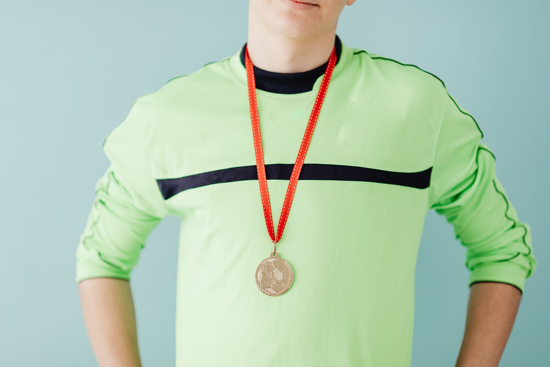 Teenager in sportswear proudly wears a gold medal with a confident pose, set against a blue background.