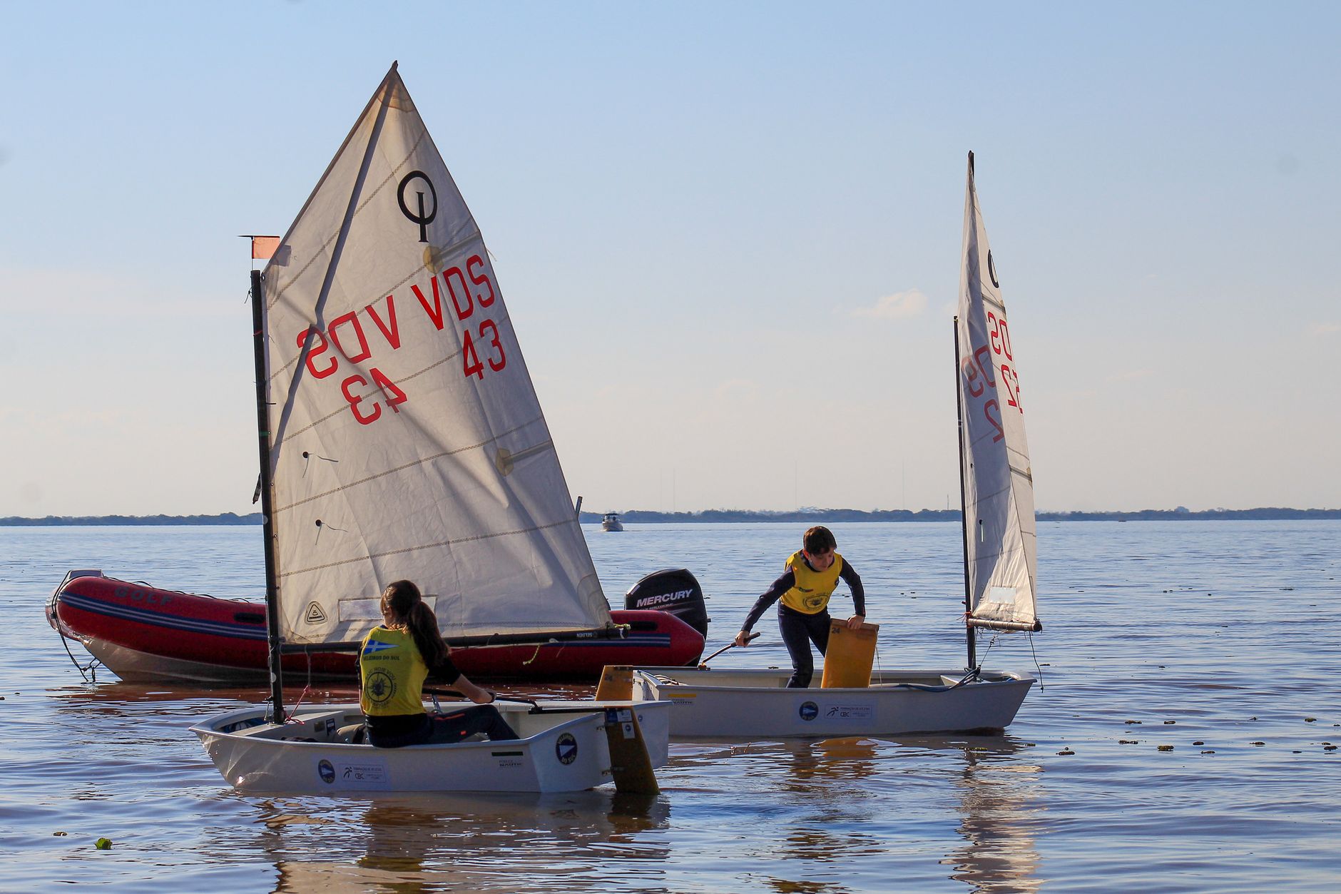 Children sailing small boats on a calm sea under a clear sky, enjoying watersports.