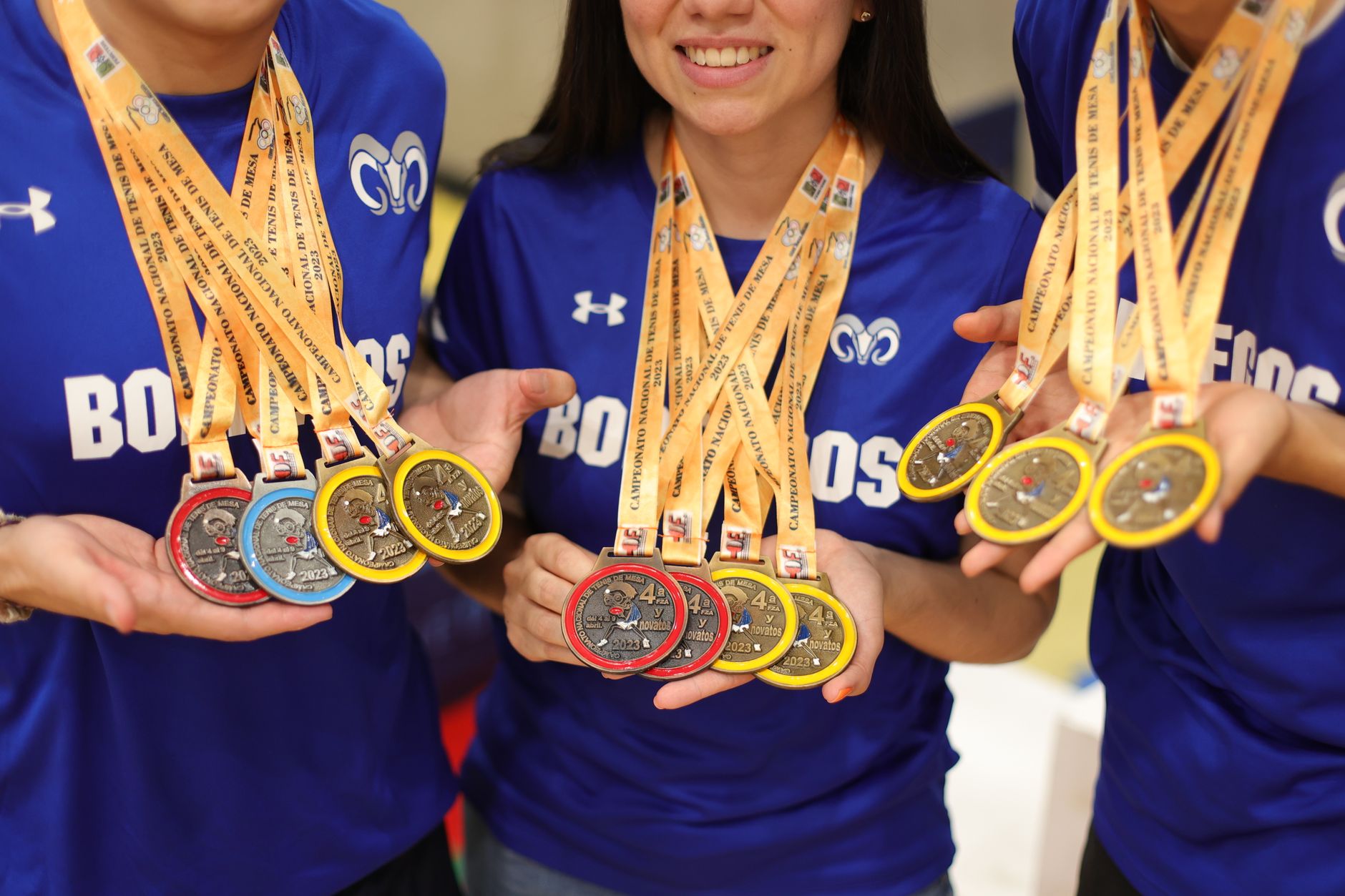 Smiling athletes in blue jerseys proudly holding multiple championship medals.