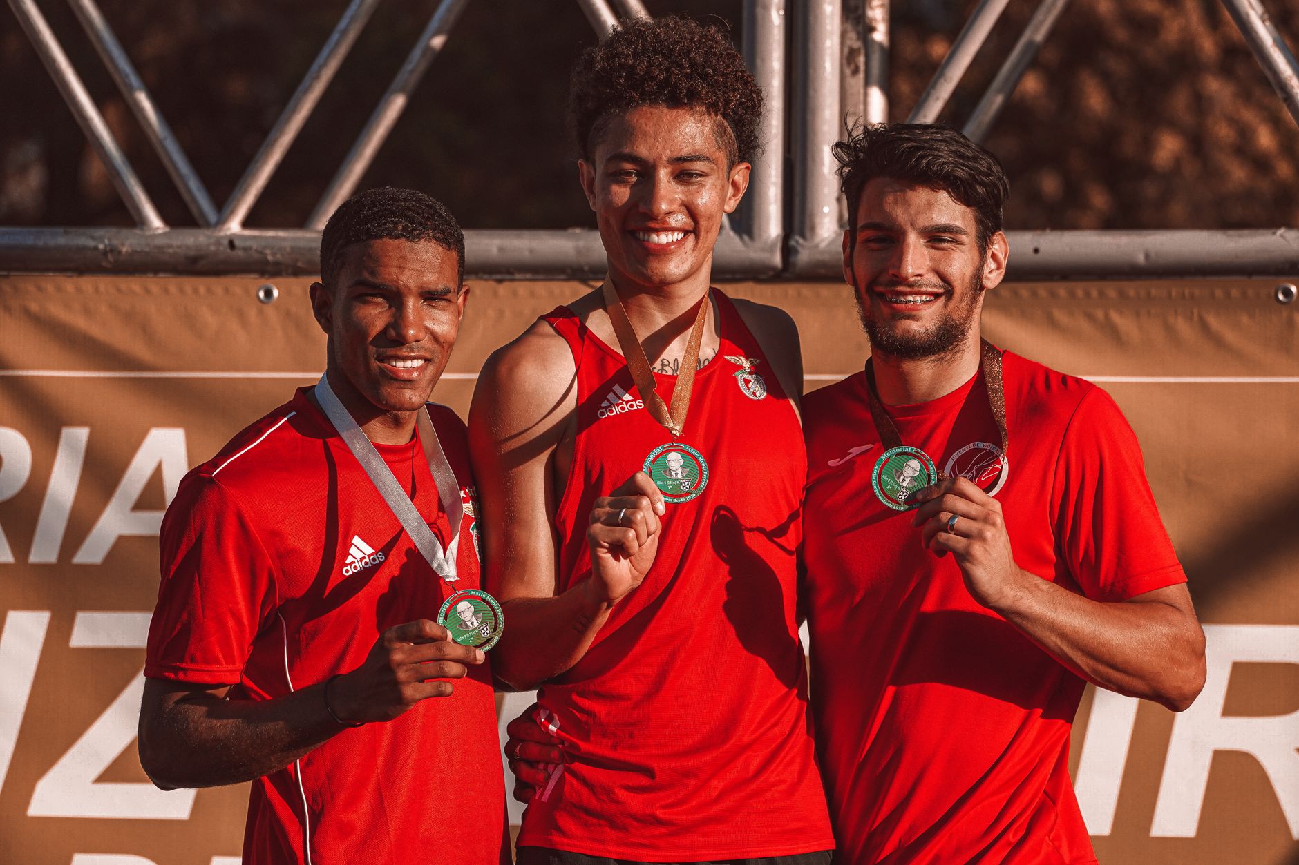 Three athletes posing with medals, smiling after a victory outdoors. Embracing team spirit.