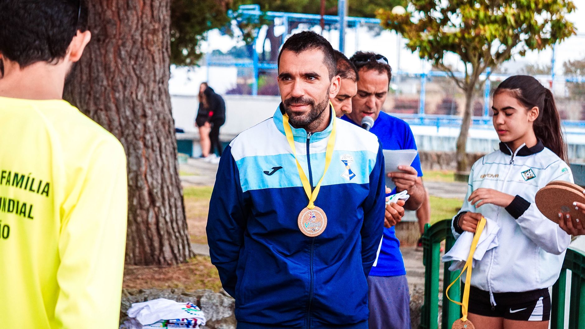 Athlete with medal at outdoor award ceremony surrounded by people in a park.