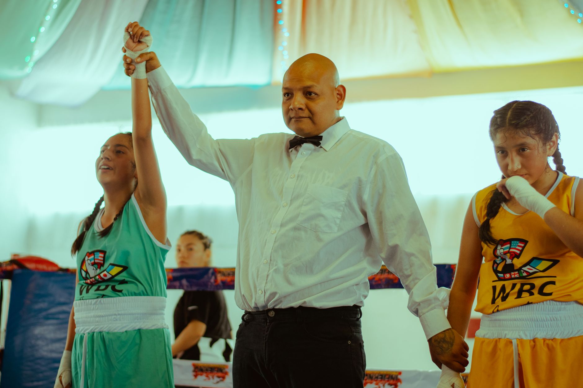 A referee announces the winner of a female boxing match in a vibrant indoor setting.