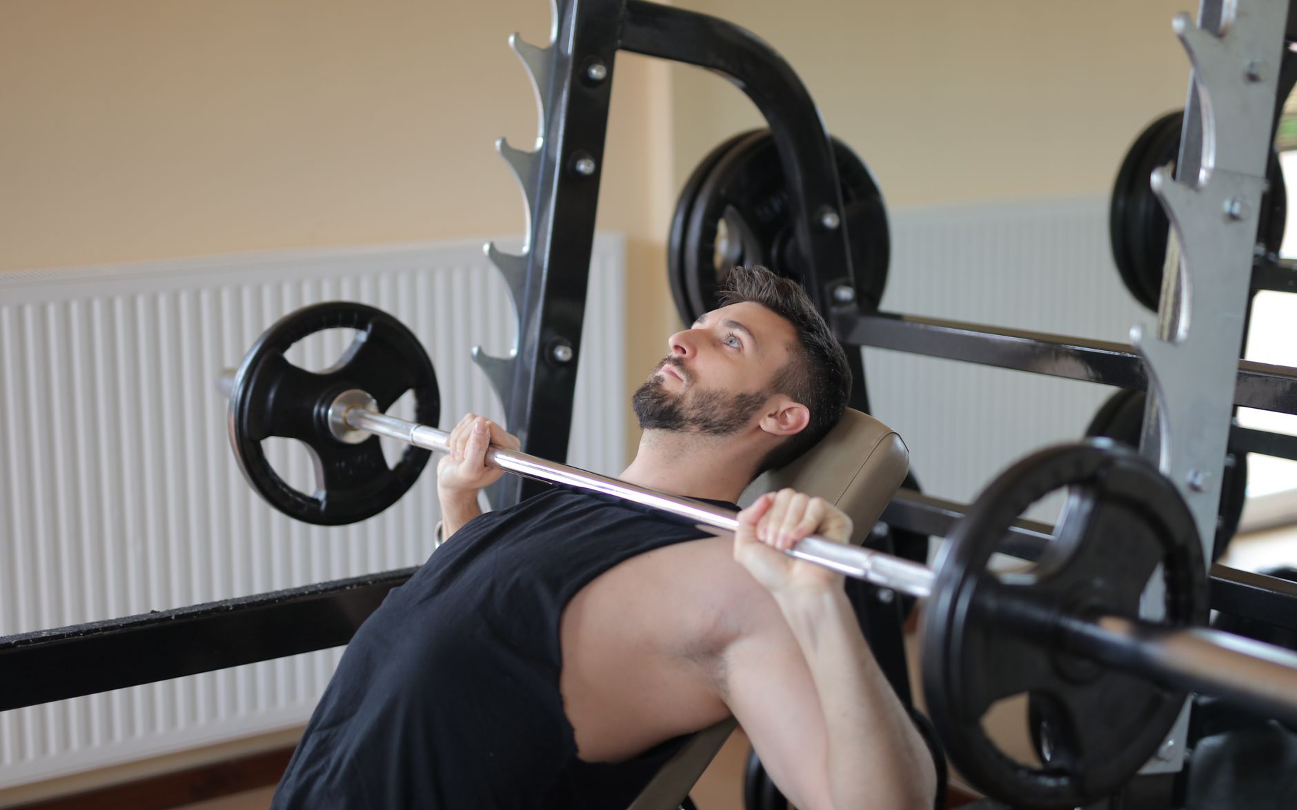 Adult man performing bench press exercise with barbell in a gym setting, showcasing strength and fitness.