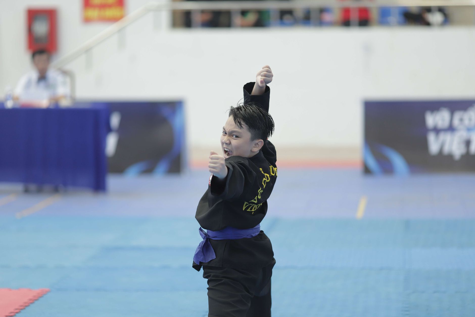 Young boy in martial arts uniform performing a pose during a competition indoors.