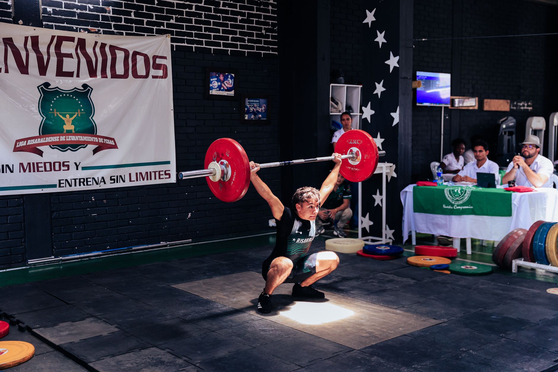 Athlete executing a snatch lift at a weightlifting competition indoors.