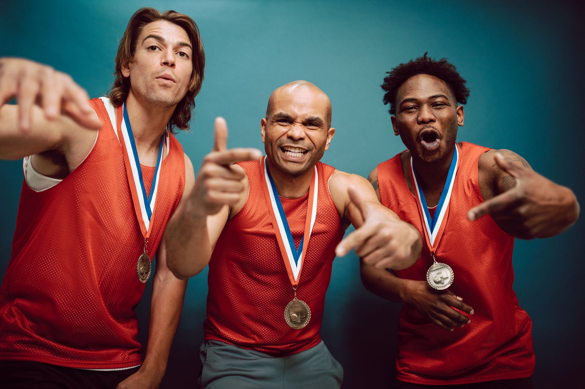 Three athletes in red jerseys celebrate with medals, showcasing team spirit.