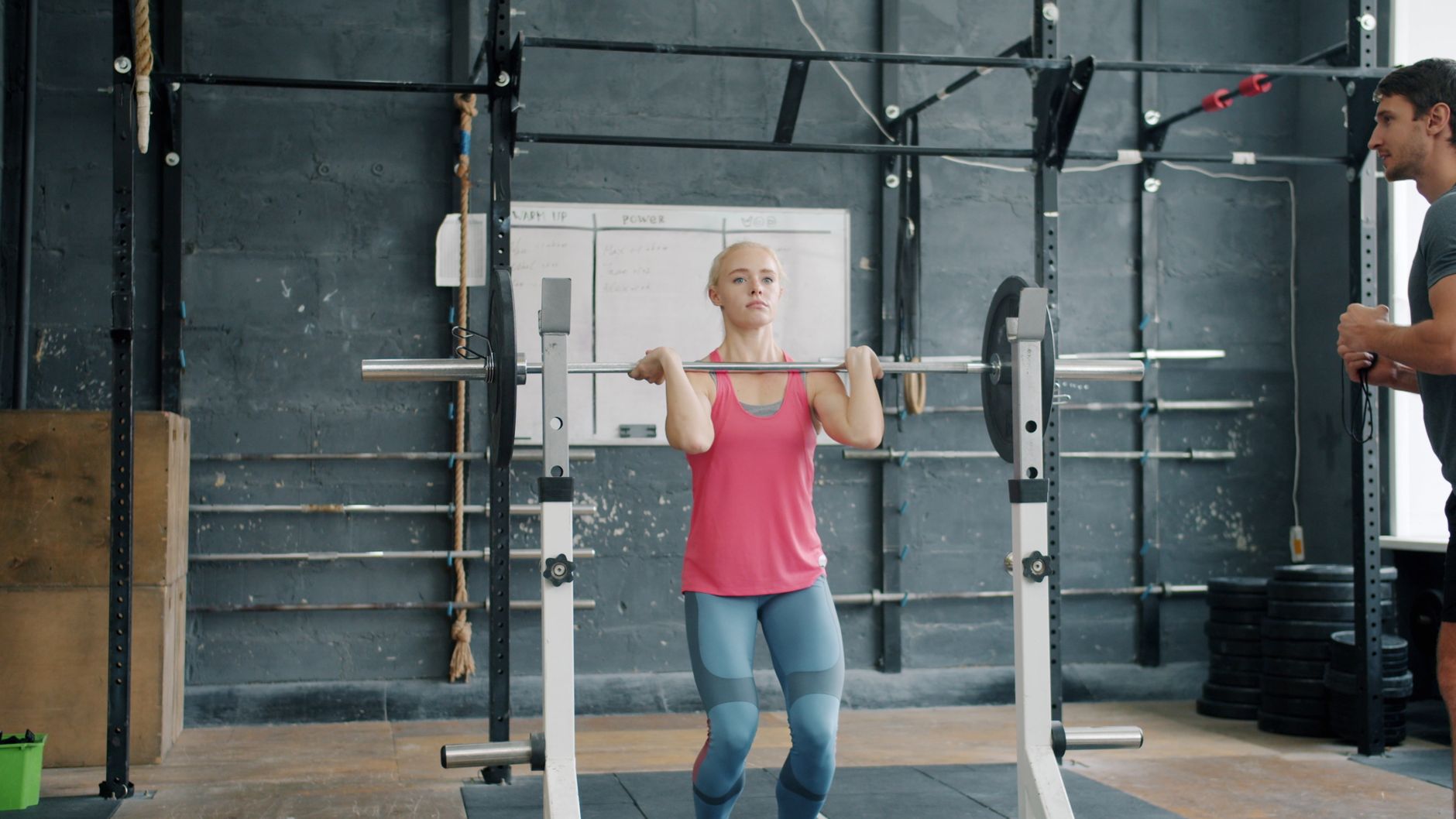 A young woman performs a barbell exercise in a modern gym interior.